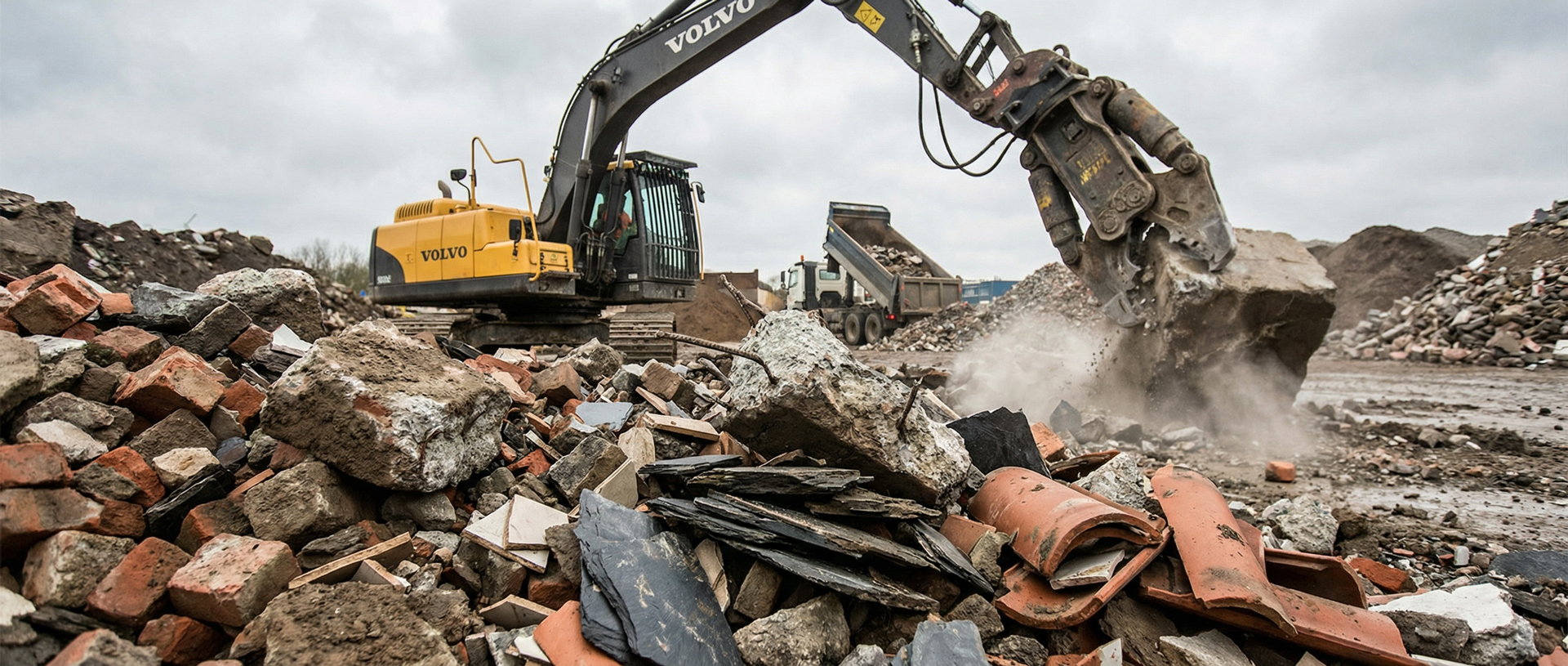 Bauschuttrecycling: Bagger zerkleinert Beton Ein gelber Bagger zerkleinert mit einem Brecher Betonbrocken auf einem Bauschutt-Recyclingplatz.