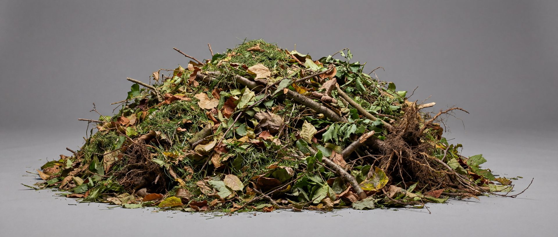 Baum- und Strauchschnitt richtig entsorgen und sortieren Ein Haufen loser Baum- und Strauchschnitt mit Laub, Rasenschnitt, Ästen und Wurzeln auf grauem Grund.